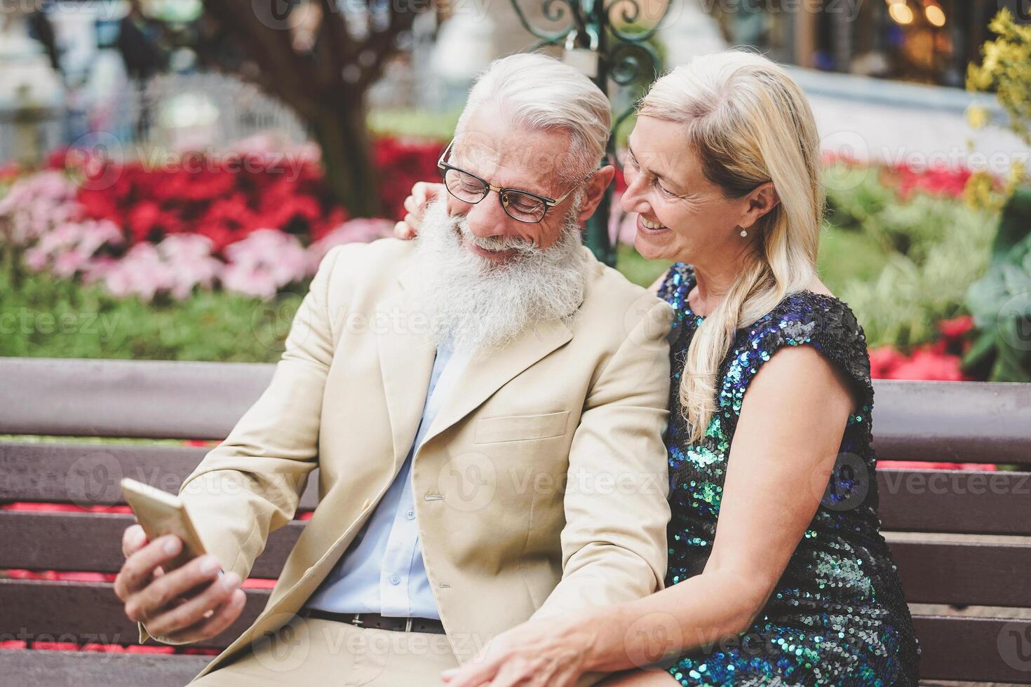 Happy senior couple watching on mobile smartphone outdoor - Mature fashion pensioners having fun with new technology cellphones apps - Social, retired, tech, elderly lifestyle concept photo