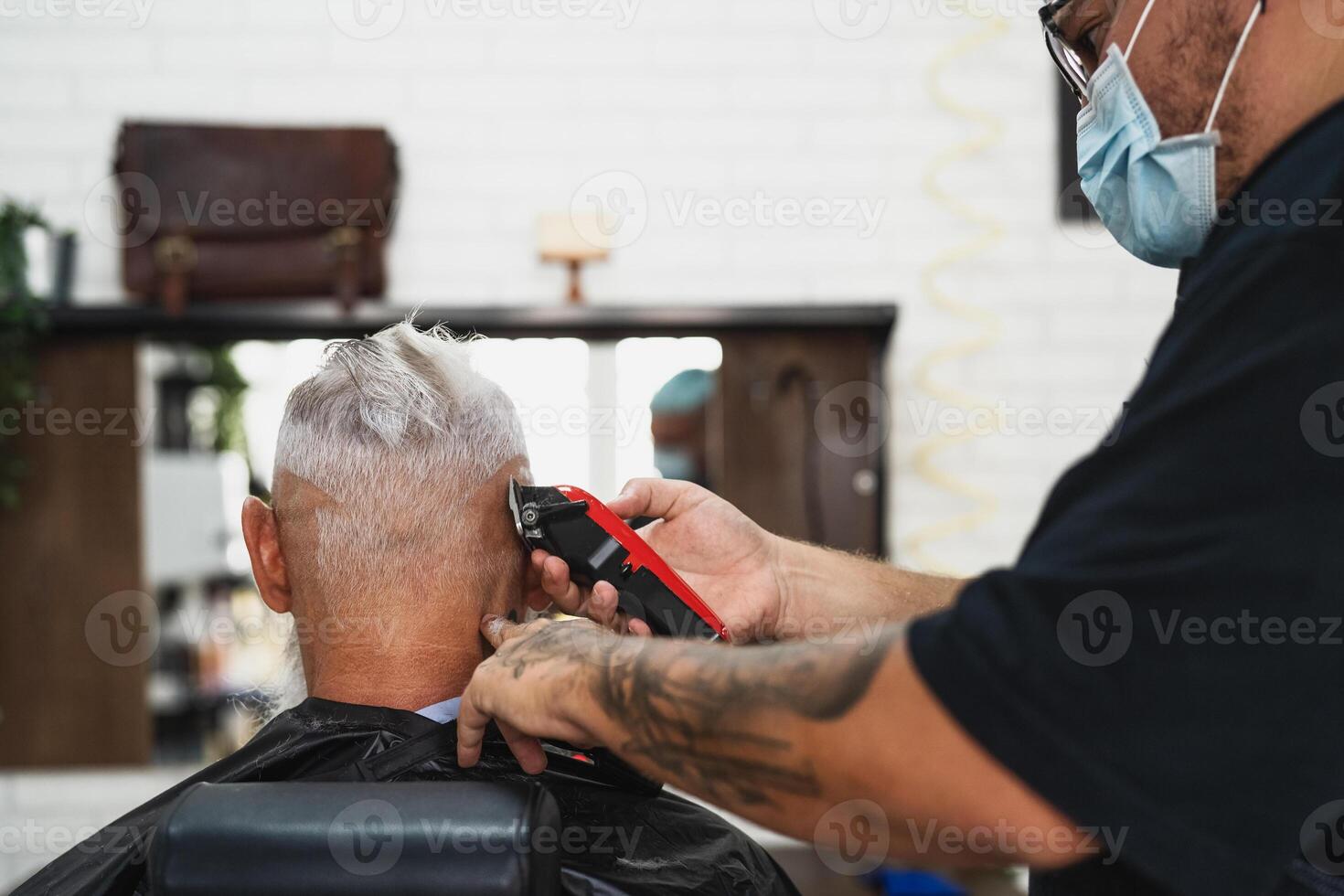 Male hairdresser cutting hair to hipster senior client while wearing face surgical mask - Young hairstylist working in barbershop during corona virus outbreak - Health care and haircut salon concept photo