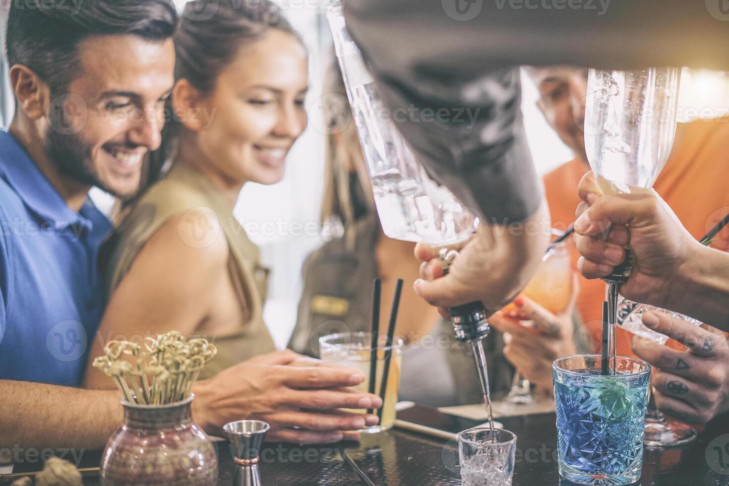 contento joven amigos teniendo divertido disfrutando bebidas a bar mientras barman preparando cócteles y Disparo - dos parejas mirando a barman microfonía alcohol bebidas - suave atención en azul vaso foto