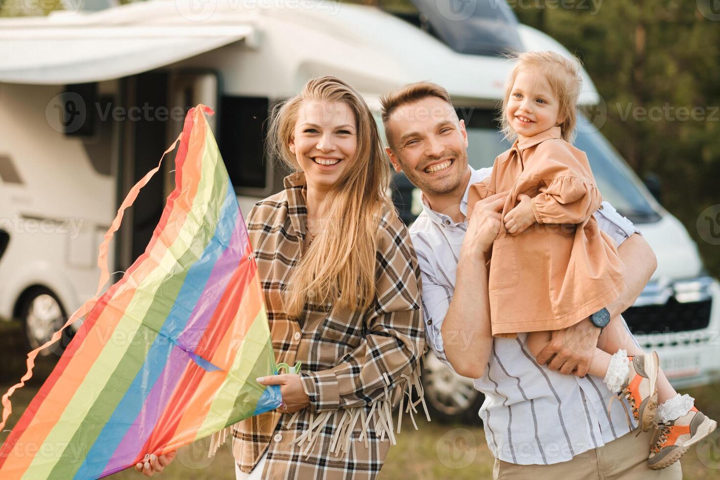 Happy parents with their child play with a kite near their motorhome in the forest photo