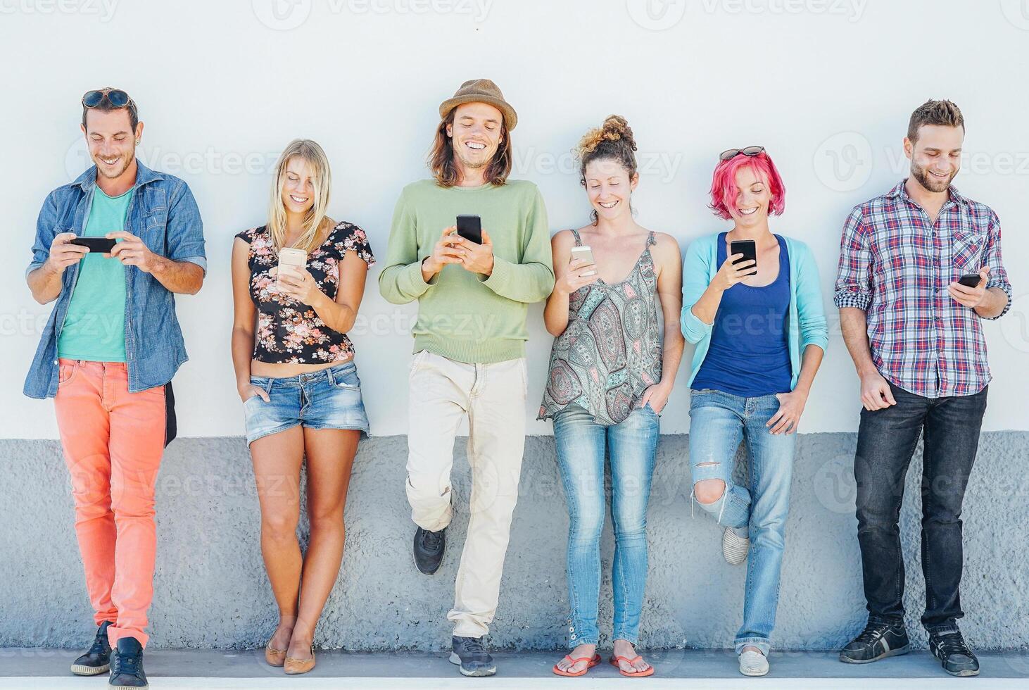 Young people watching on their smart mobile phones leaning on a wall - Generation addicted to new technology - Concept of youth addiction to social network trends photo