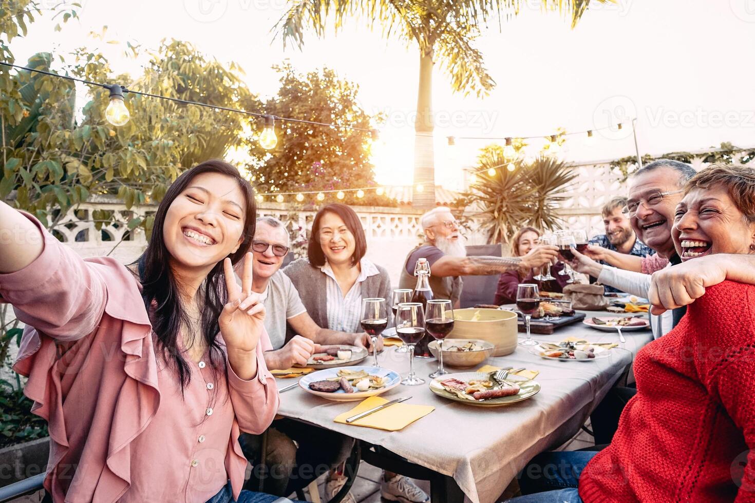 Happy family cheering and toasting with red wine glasses at dinner outdoor - People with different ages and ethnicity  having fun at bbq party - food and drink, retired and young people concept photo