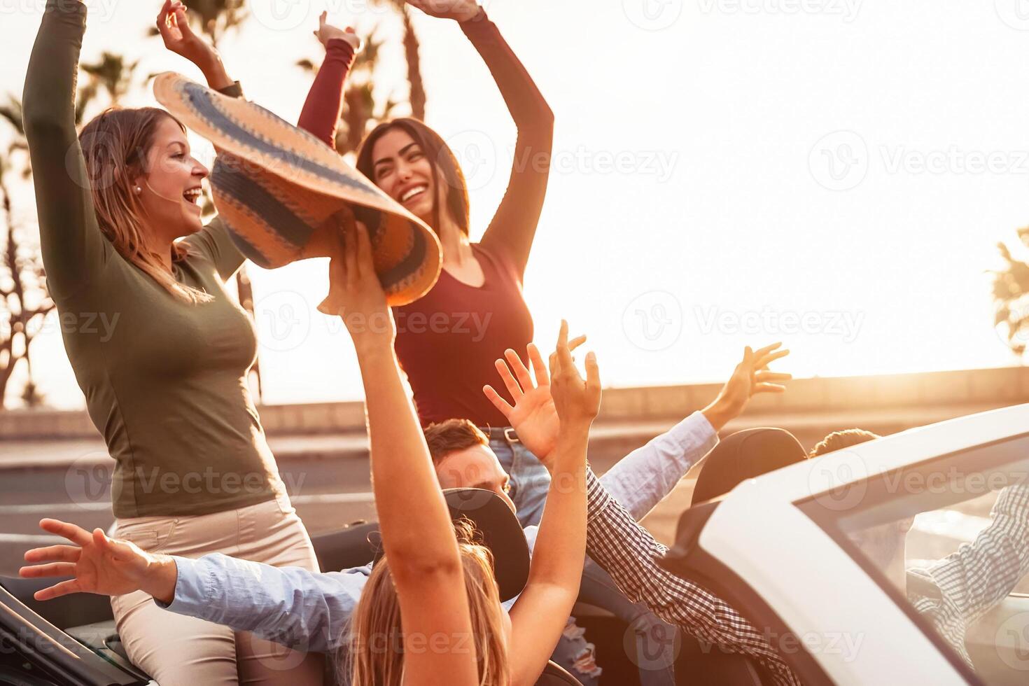 Happy friends having fun on convertible car in road trip - Group young people enjoying vacation together in tropical city - Youth culture lifestyle and travel transportation concept photo