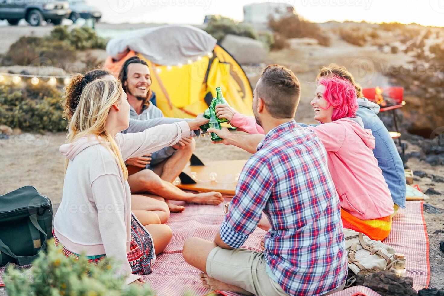 Happy friends toasting with beers at barbecue dinner on the beach - Young people camping with tent having fun cheering and drinking beer - Friendship and youth lifestyle vacation concept photo
