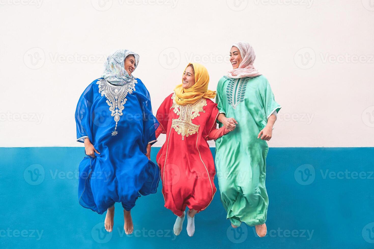 Happy muslim women jumping together outdoor - Arabian teen girls having fun in the city - concept of people,costume, culure and religion photo