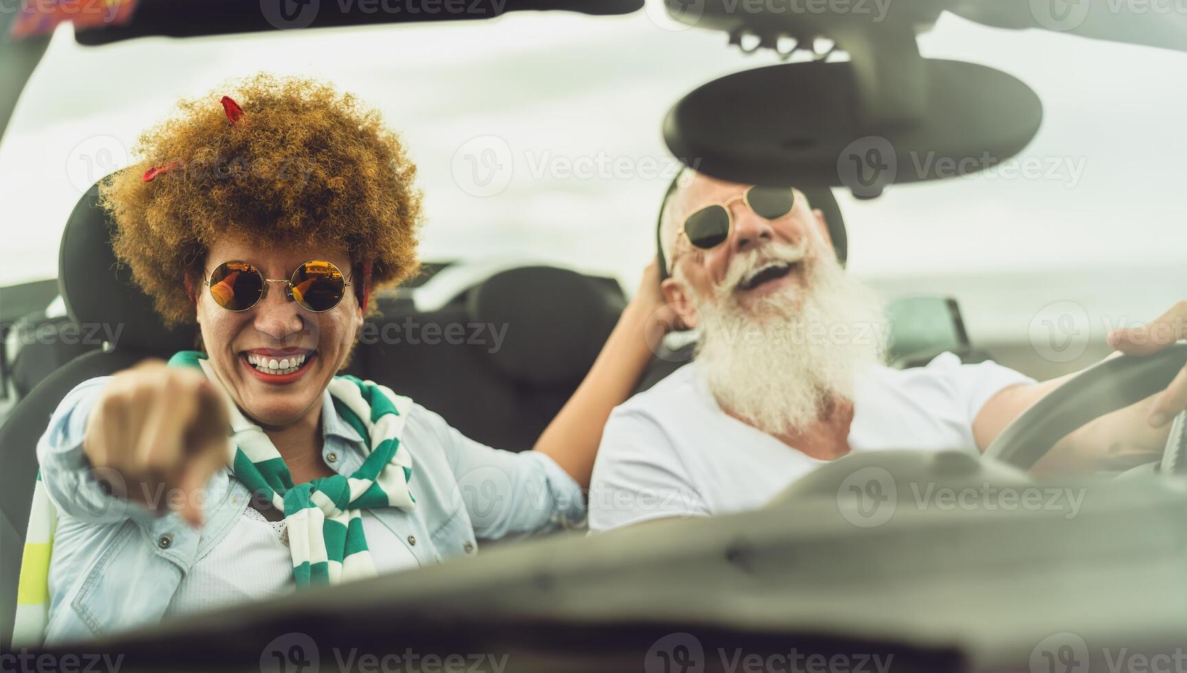 Happy senior couple having fun driving on new convertible car - Mature people enjoying time together during road trip tour vacation - Elderly lifestyle and travel culture transportation concept photo