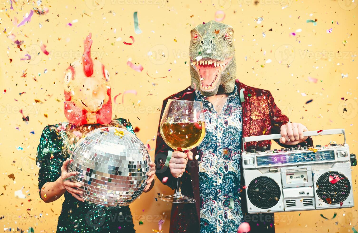 Crazy couple celebrating new year eve wearing chicken and dinosaur t-rex mask - Young trendy people having fun drinking champagne and listening music with vintage boombox - Absurd and holidays concept photo