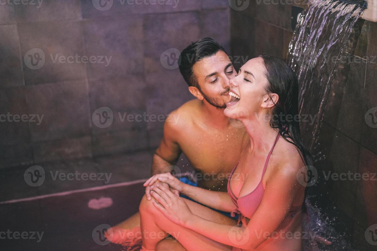 Young couple of lovers enjoying the pool waterfall hotel resort spa - Loving teenagers having fun and relaxing at wellness spa day - Man giving a kiss to his girlfriend - Concept of relax and love photo