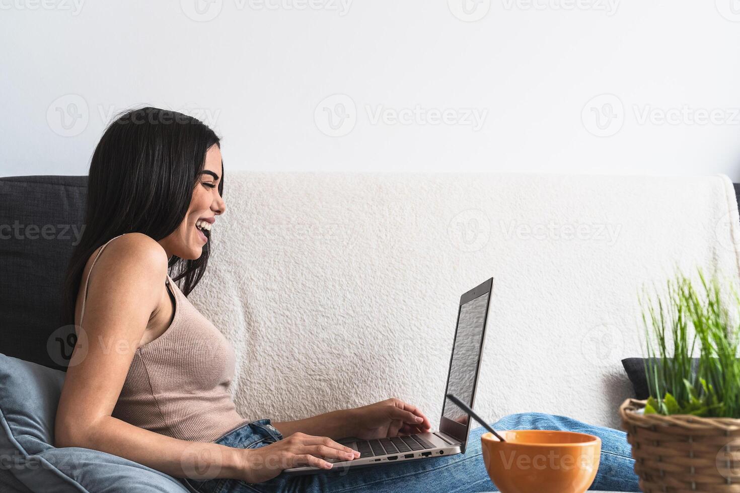 Young woman using laptop on sofa - Happy girl having fun in computer video call at home - Youth millennial people and technology concept photo