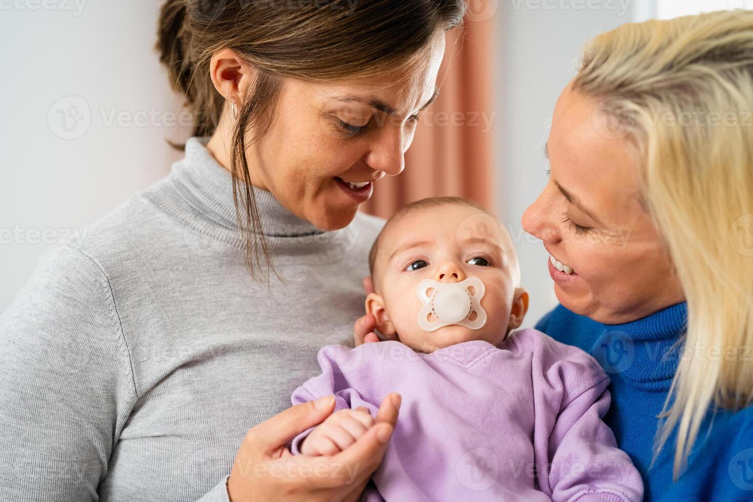 Happy lesbian couple having tender moments with their small baby at home - Family and maternity concept photo