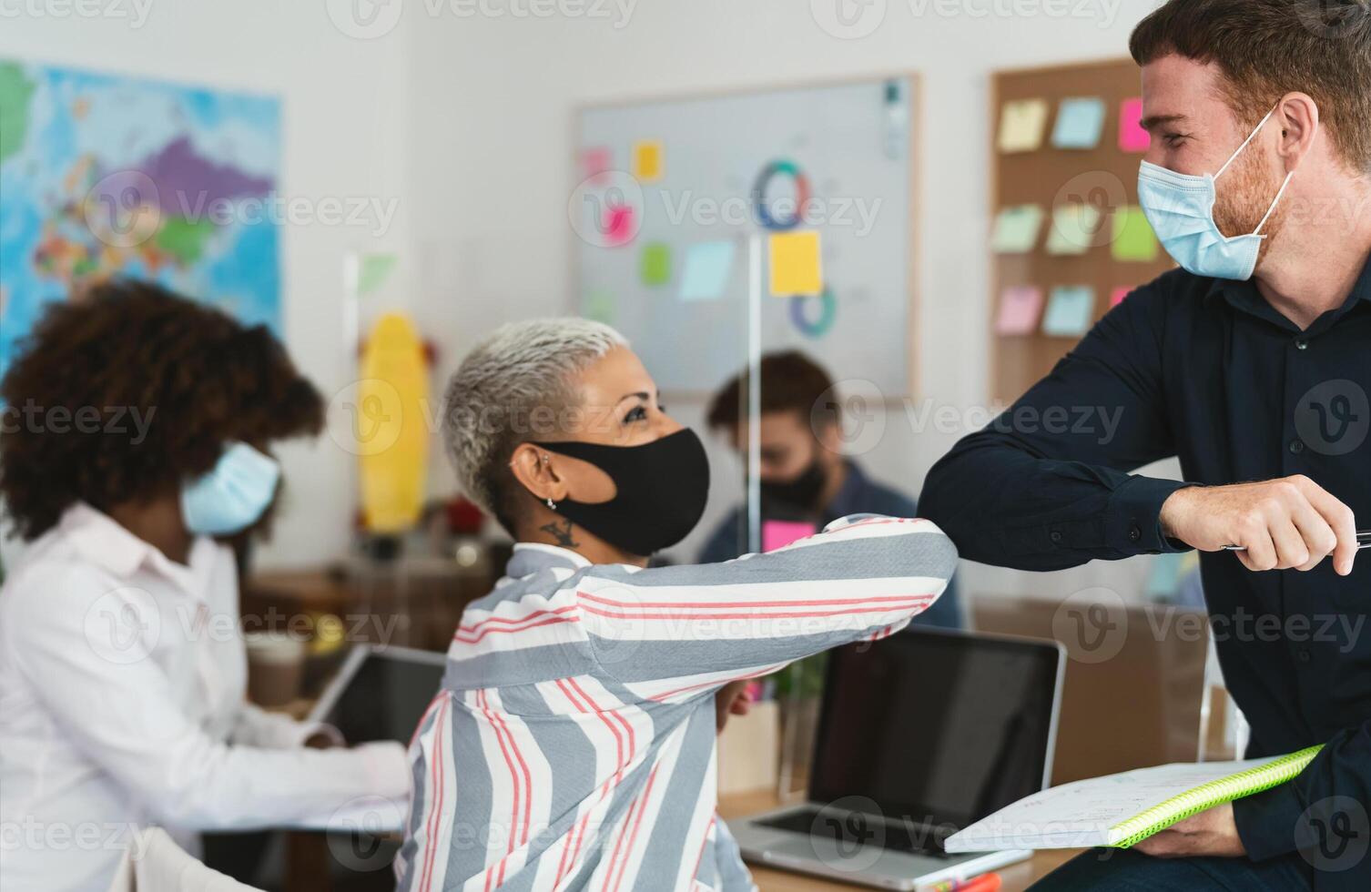 joven multirracial trabajadores vistiendo cara máscara haciendo nuevo social distancia saludos golpeando codos dentro trabajo colaborativo creativo espacio foto