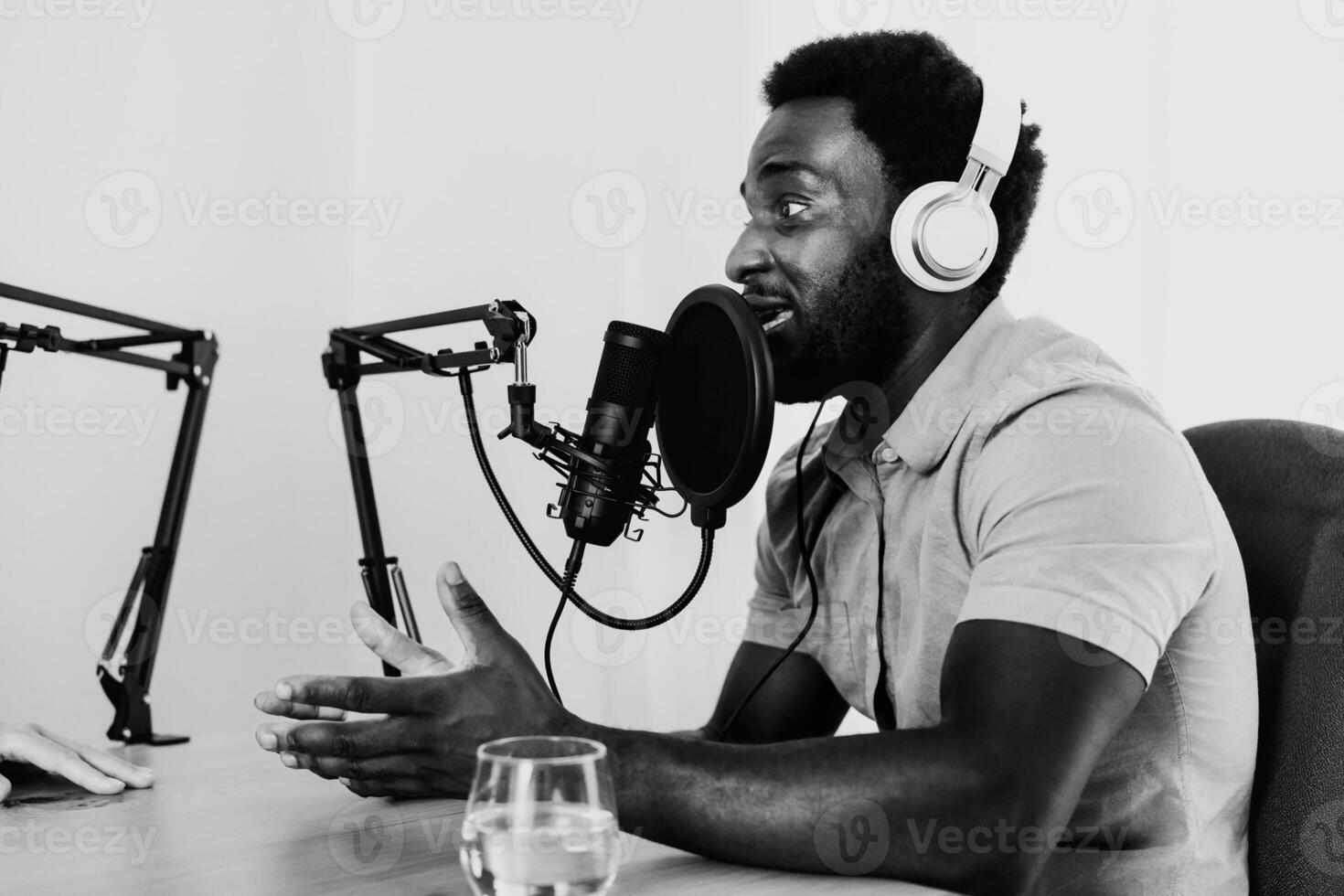 African man recording a podcast using microphone and headphones from his home studio - Black and white editing photo