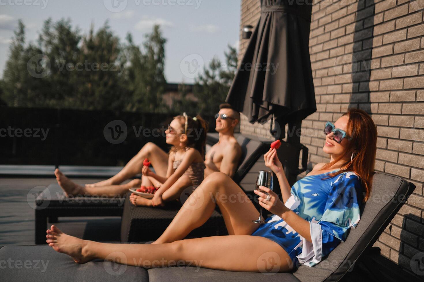 un contento familia en trajes de baño tomar el sol en verano en su terraza en Dom camas foto