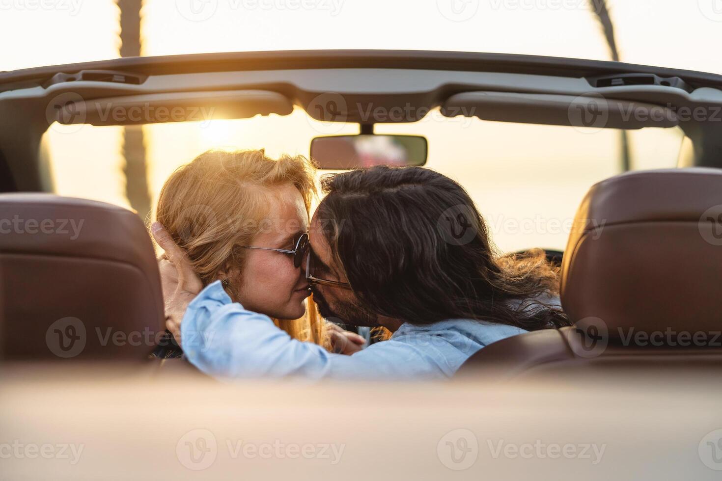 Happy couple kissing in convertible car - Romantic people having tender moment during road trip in tropical city - Love relationship and youth vacation lifestyle concept photo