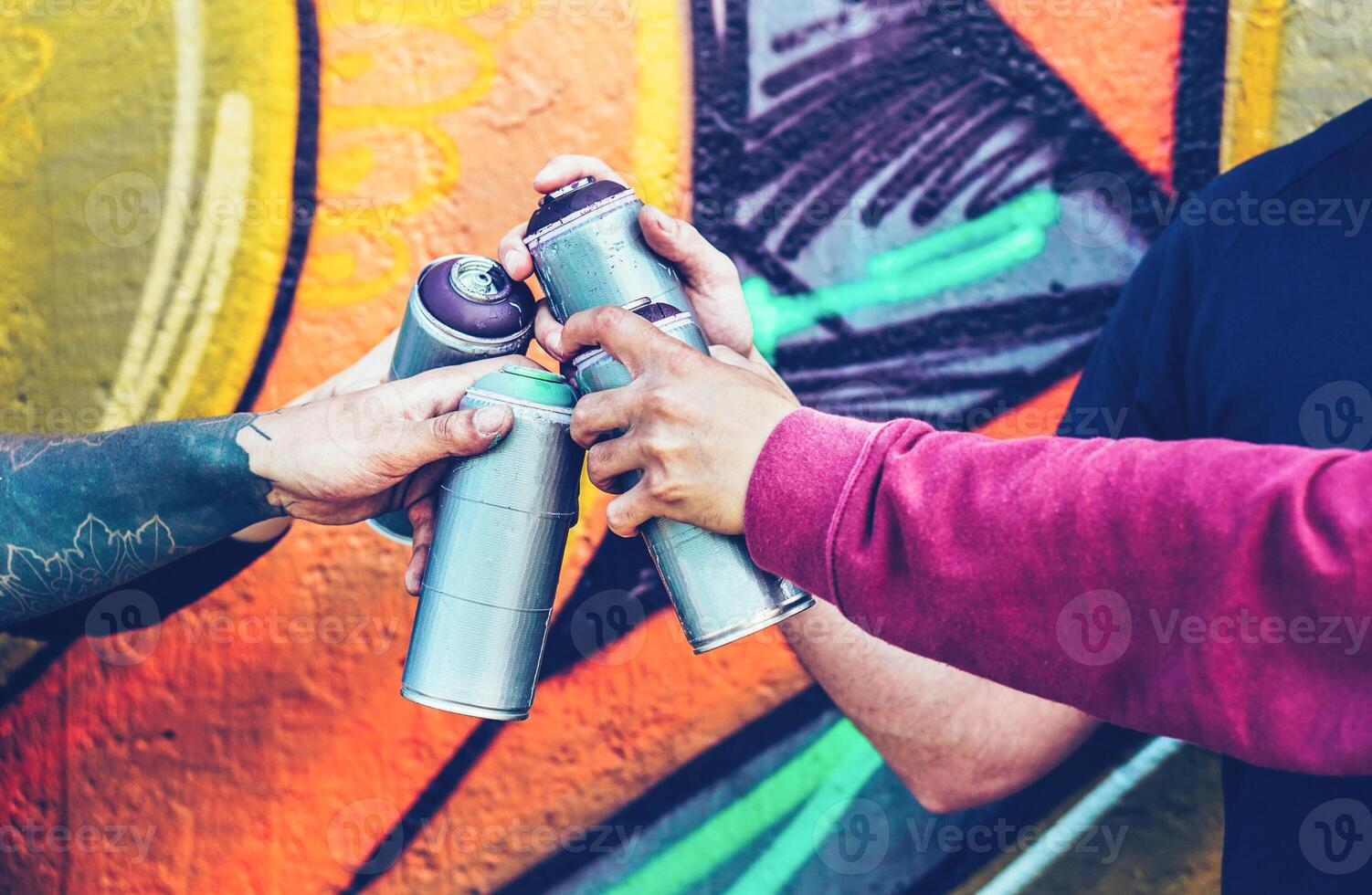 Group of graffiti artists stacking hands while holding spray color can against mural background - Young painter at work - Concept of contemporary art, street art and people youth lifestyle photo