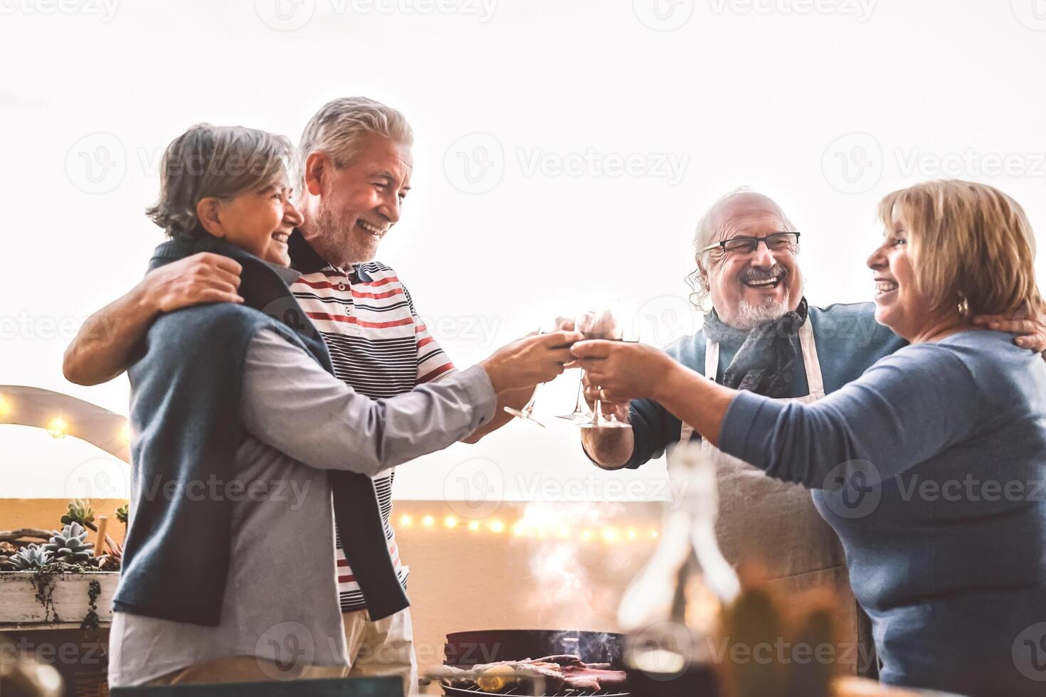 Happy senior friends drinking red wine at barbecue on house patio  - Mature people cheering and dining together at bbq party - Food and elderly friendship lifestyle concept photo