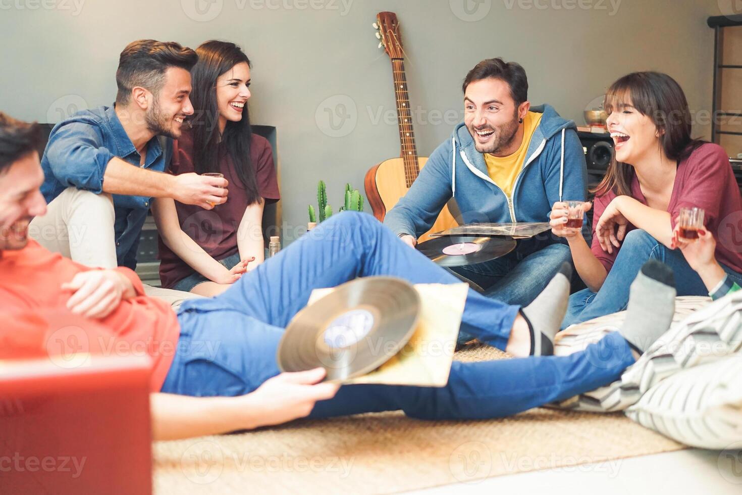 Group of happy friends doing party listening vintage vinyl disc at home - Young people having fun drinking shots and laughing together in their apartment - Friendship, music, youth lifestyle holidays photo