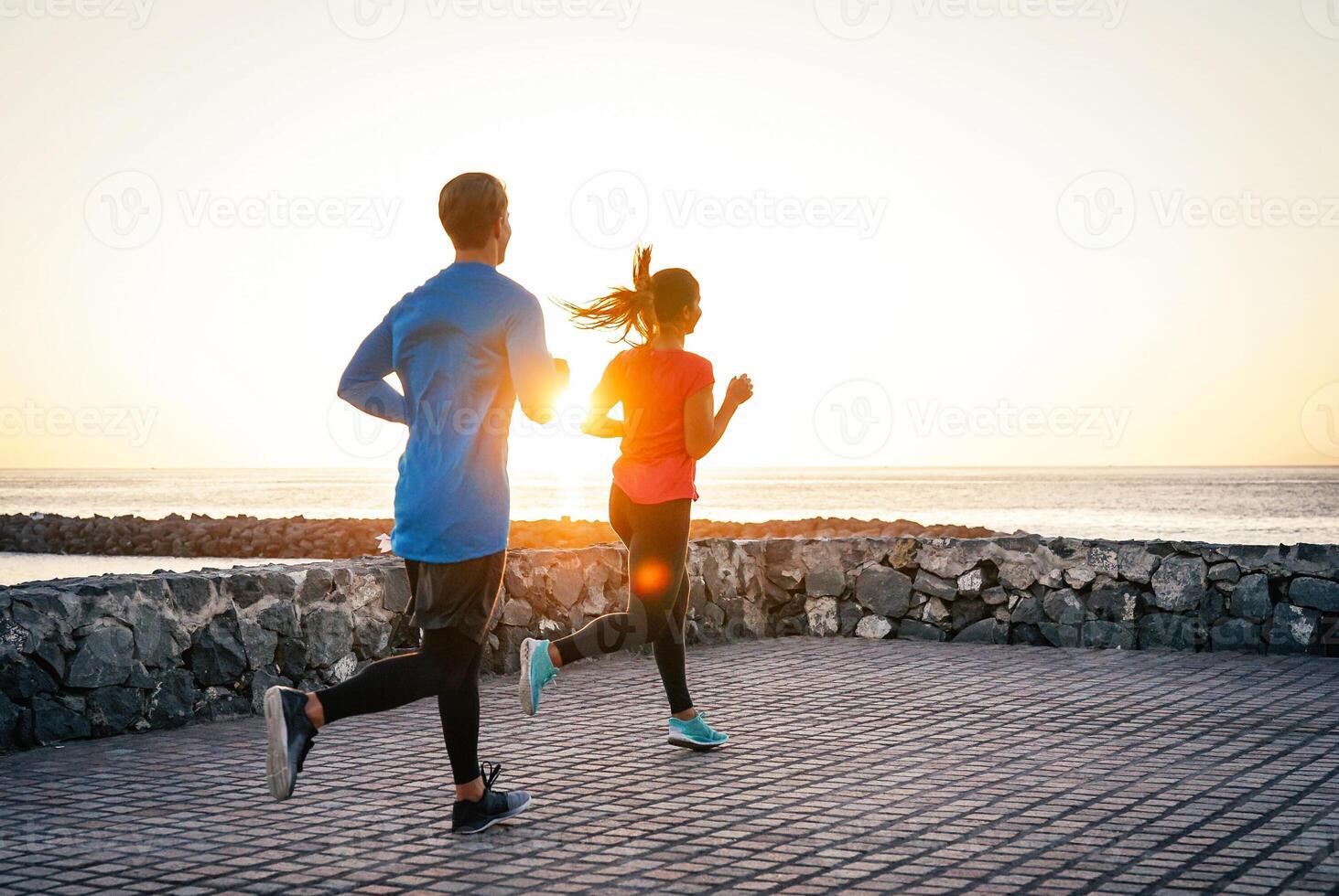 Health young couple jogging together next the ocean during a magnificent sunset - People work out on the beach - Relationship, sport, lifestyle concept photo