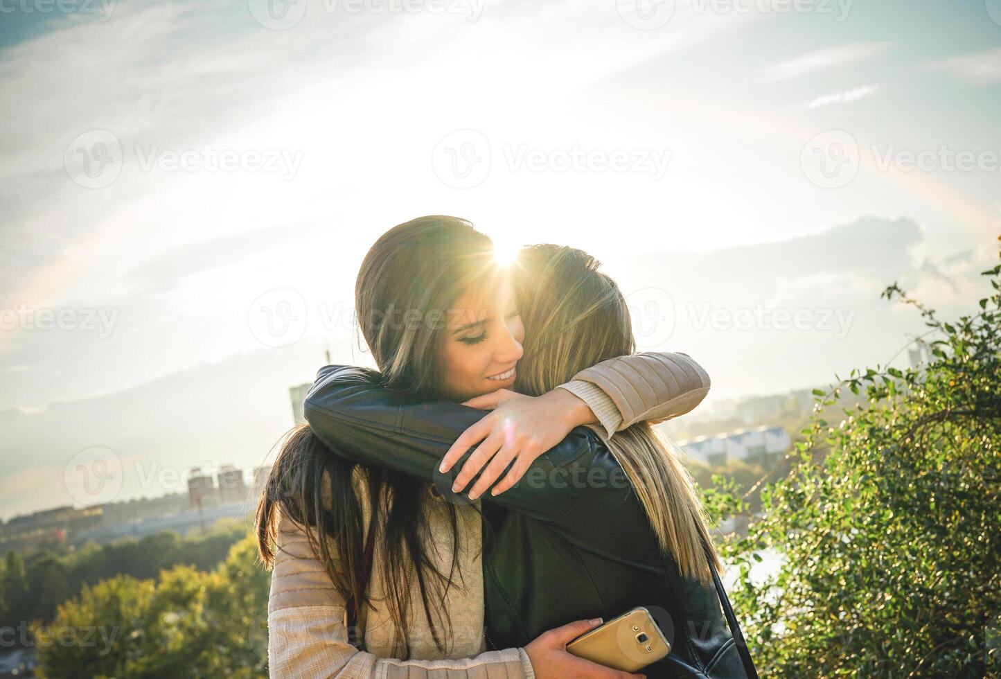 Happy meeting of two friends hugging at sunset outdoor - Pleasant moment of young sisters embracing in the wilderness as the sun shines upon them - Vignette editing photo