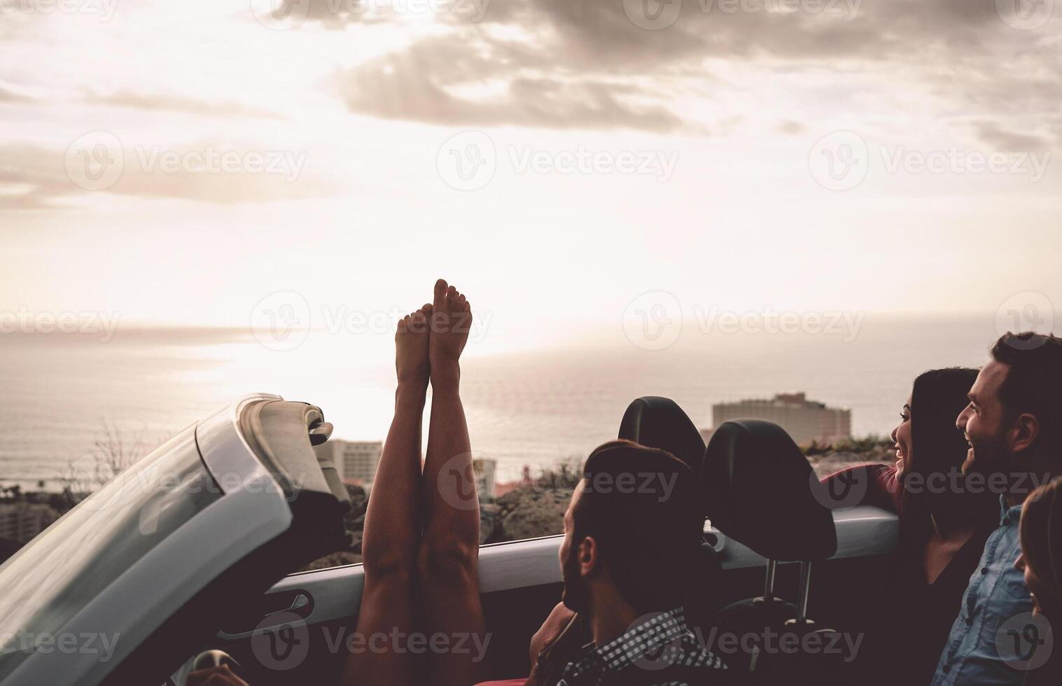 Happy friends driving on convertible car at sunset - Young people having fun during vacation road trip in cabriolet - Friendship, travel and youth lifestyle concept photo