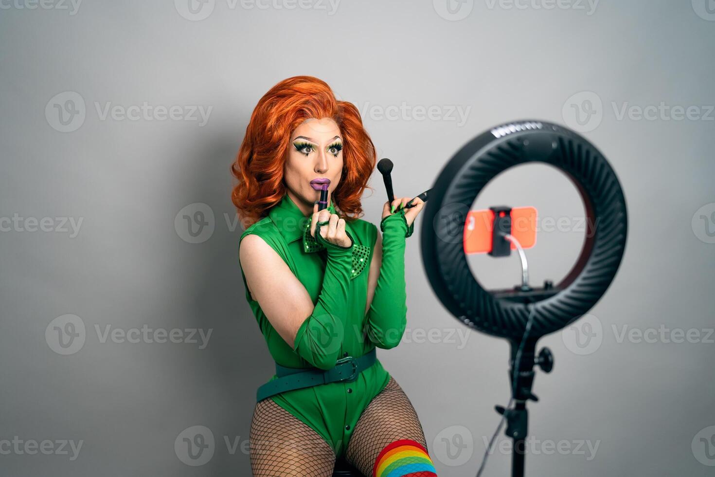 Happy drag queen social influencer vlogging online a makeup class with smartphone cam and ring led photo