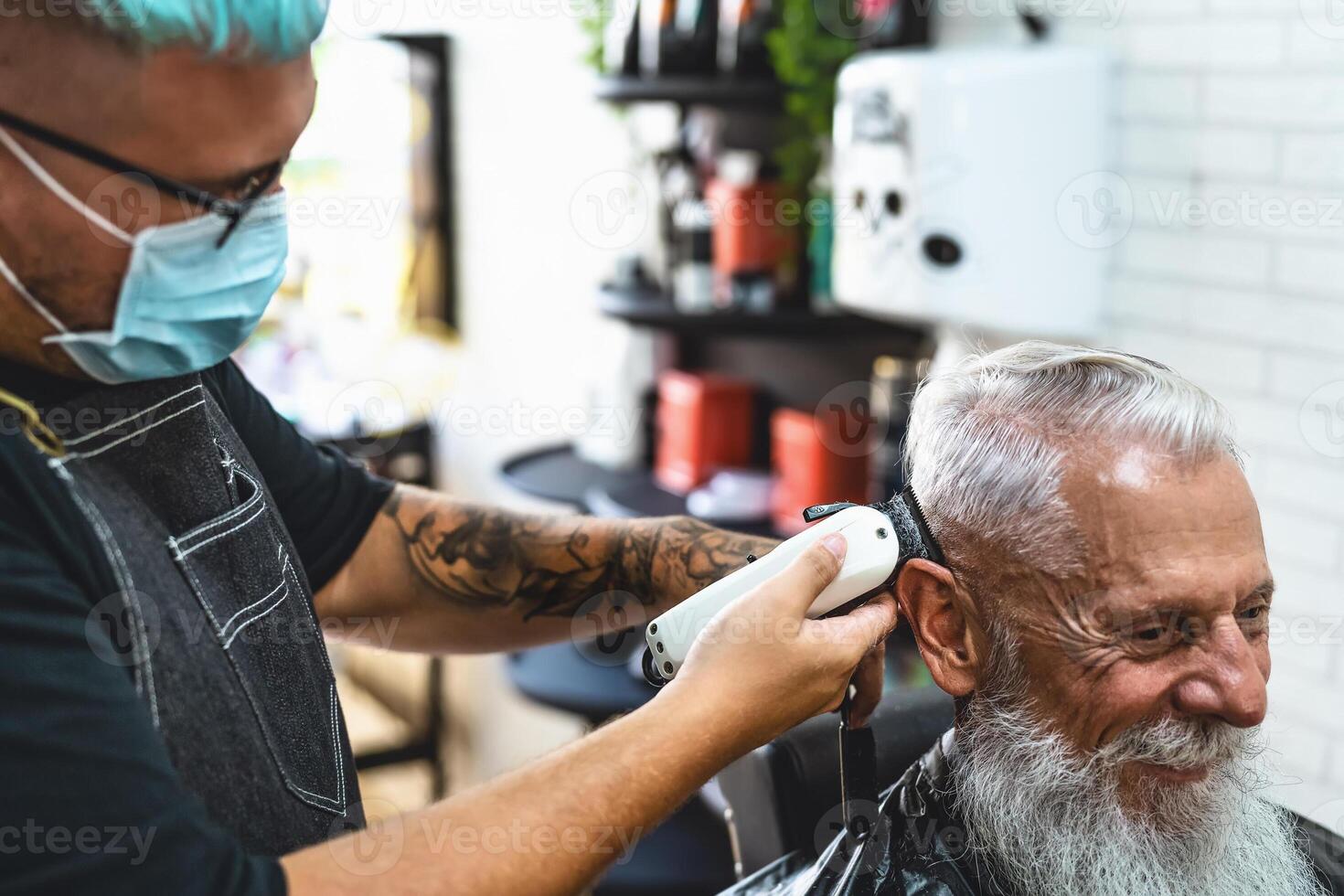 Male hairdresser cutting hair to hipster senior client while wearing face surgical mask - Young hairstylist working in barbershop during corona virus outbreak - Health care and haircut salon concept photo