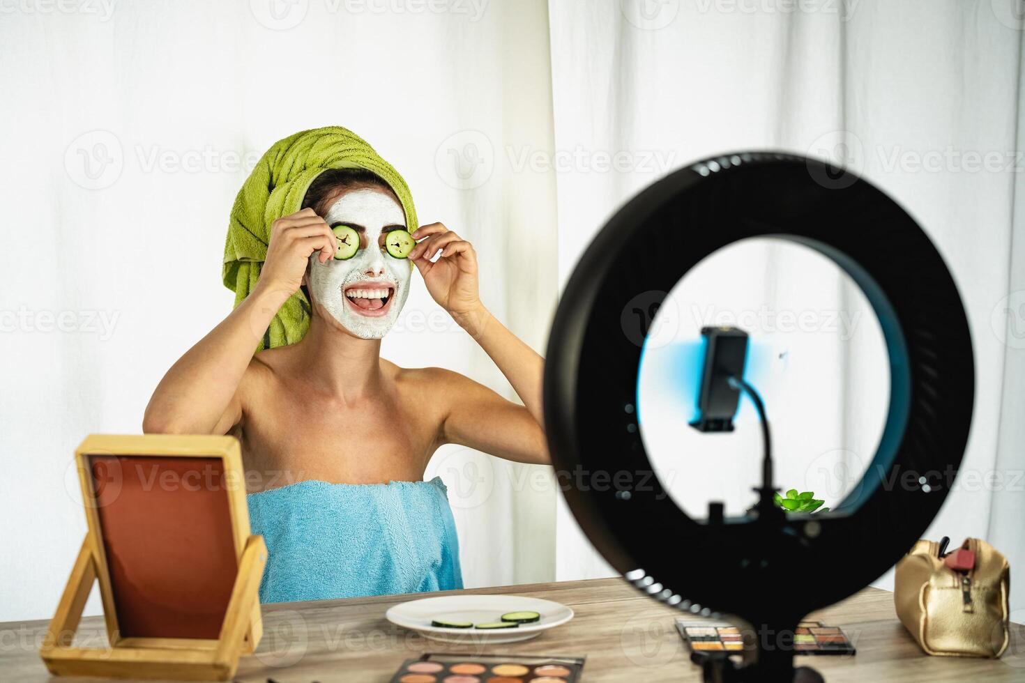 Young female vlogger applying skincare facial mask while streaming live for web channel at home - Happy girl having fun filming tutorial with mobile smartphone - Social influencer lifestyle concept photo