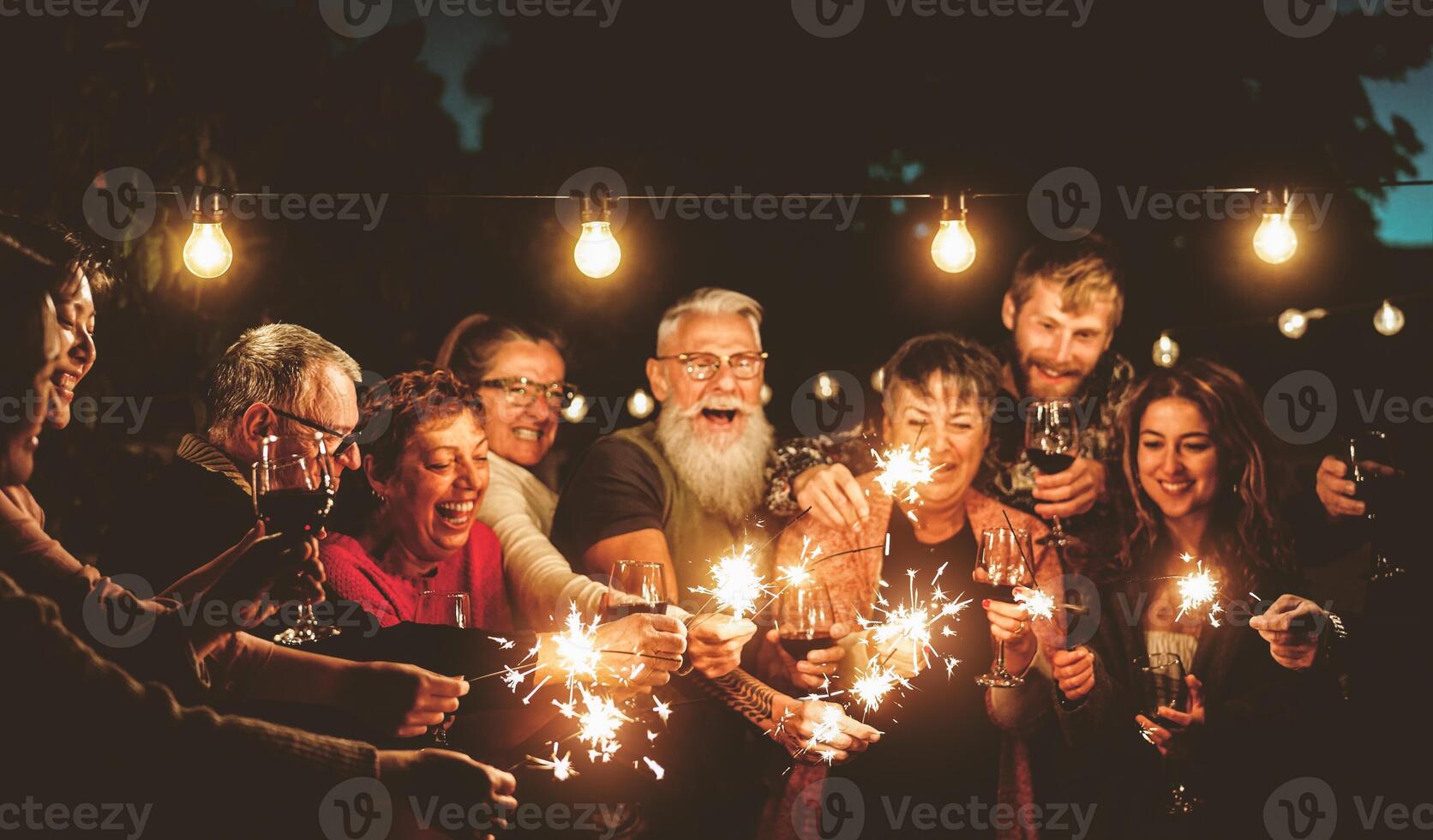 Happy family celebrating with sparklers fireworks at night party - Group of people with different ages and ethnicity having fun together - Holidays lifestyle concept photo