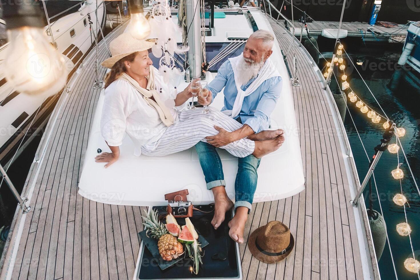 Senior couple toasting champagne on sailboat vacation - Happy mature people having fun celebrating wedding anniversary on boat trip - Love relationship and travel lifestyle concept photo