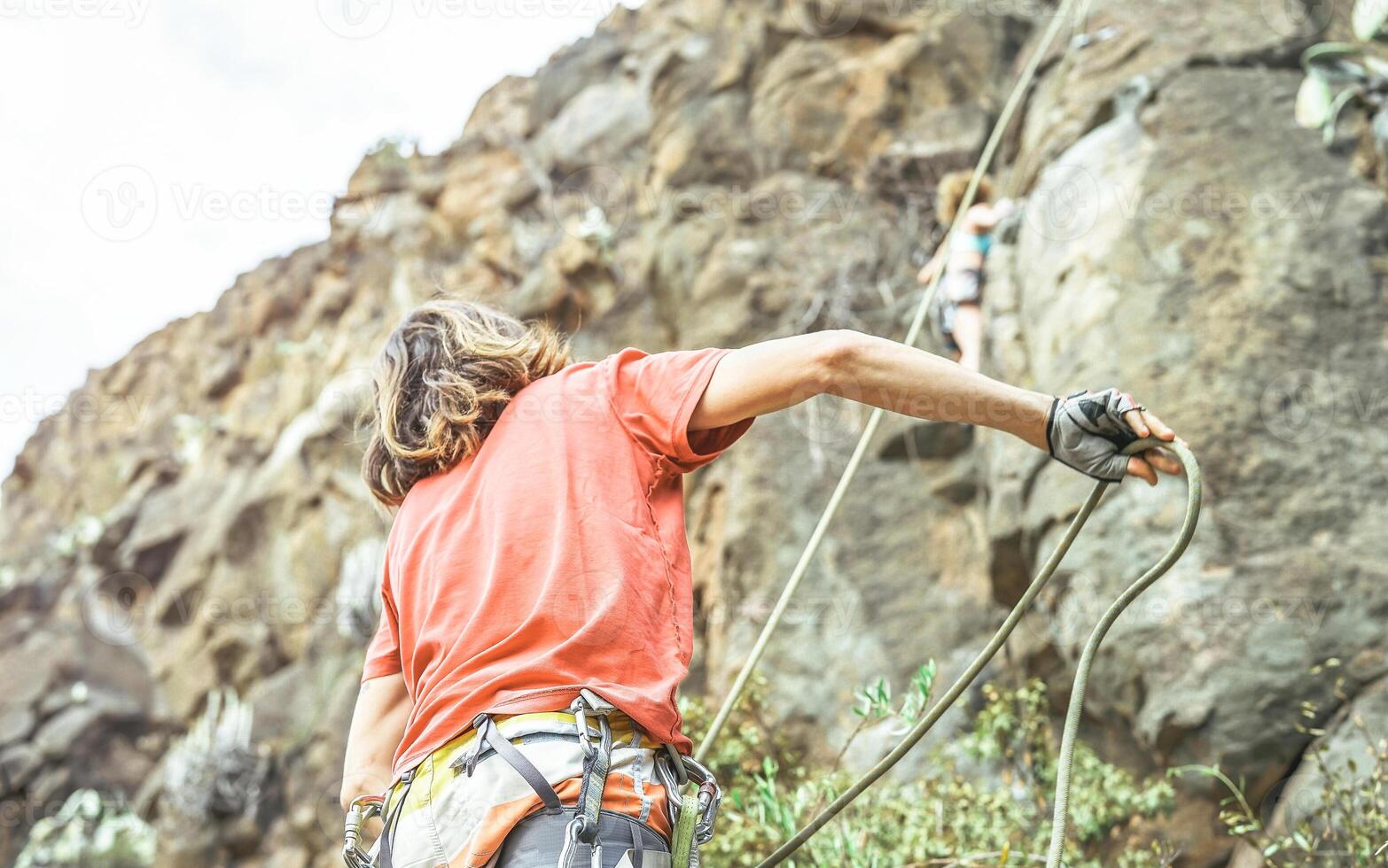 Man giving security to woman who is climbing up on mountain cliff - Climber in action on the rock near the peak - concept of extreme lifestyle, adrenaline and sport photo