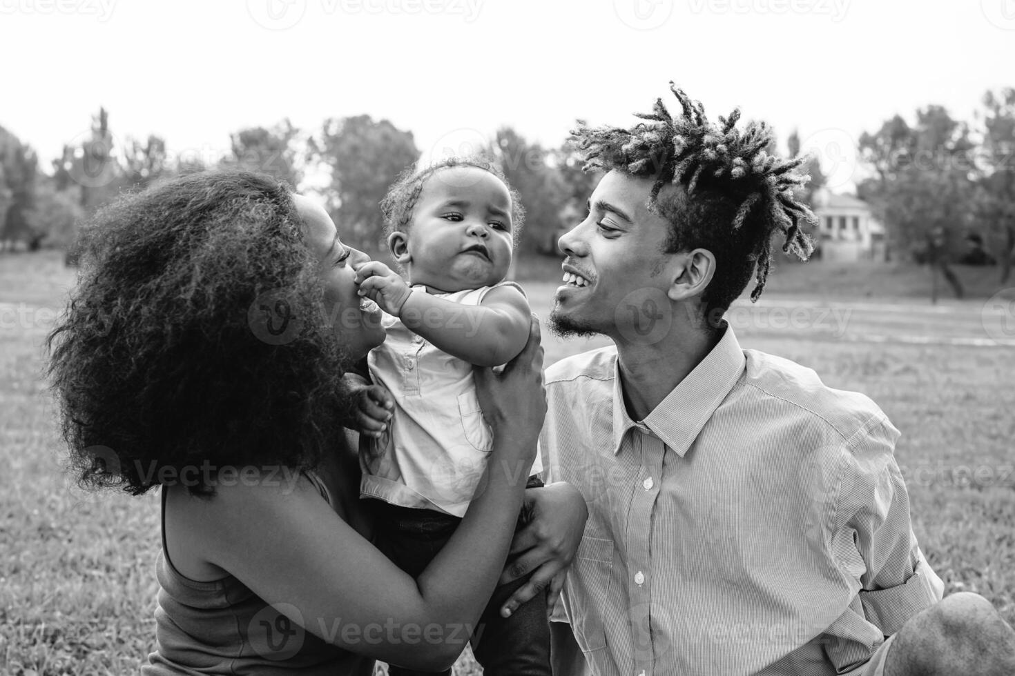 Happy African family enjoying a tender moment during the weekend outdoor - Mother and father having fun with their daughter in a public park - Love, parents and happiness concept photo