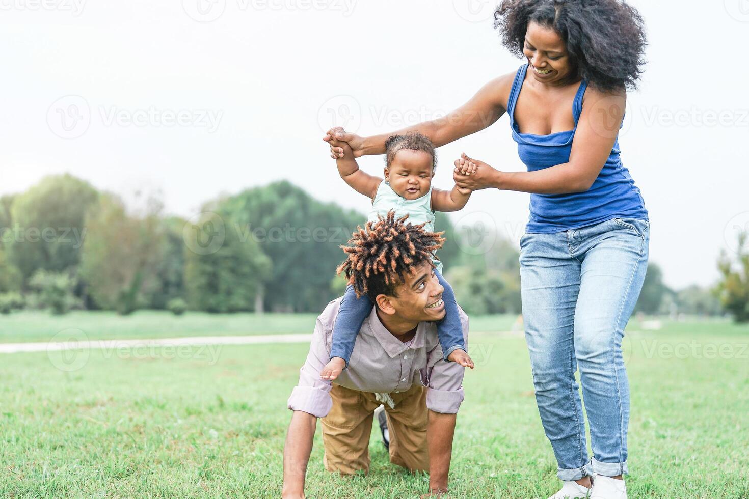 Happy african family having fun in a public park outdoor - Mother and father playing with their daughter during a weekend sunny day - Love and concept happiness photo