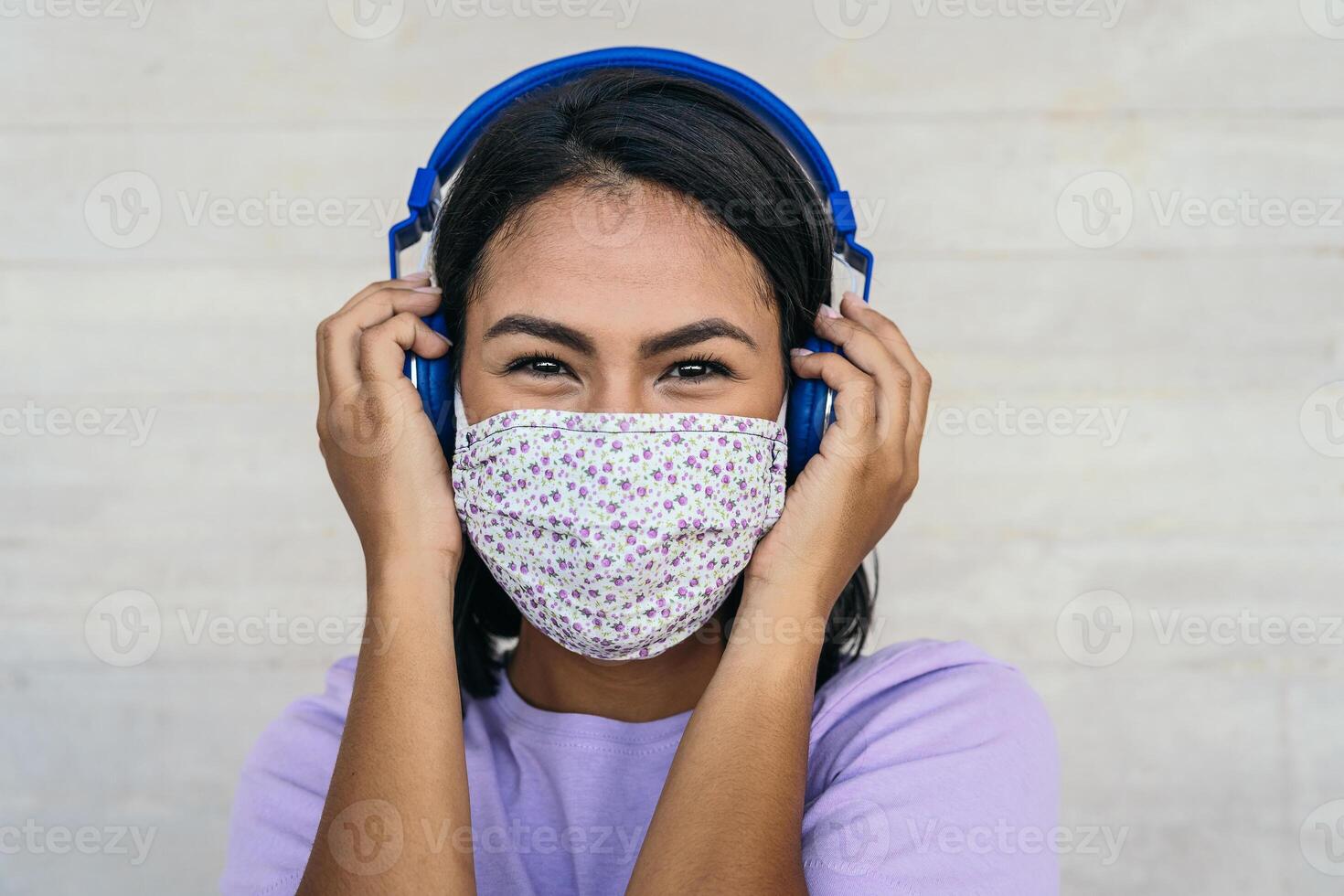 Young woman wearing face mask listening to music with wireless headphones - Latin girl using protective facemask for preventing spread of corona virus - Outbreak health care and technology concept photo