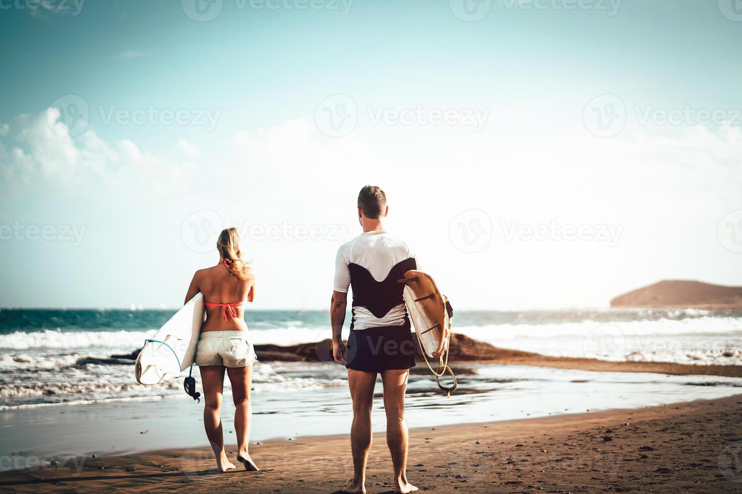 Pareja de surfistas en pie en el playa con tablas de surf preparando a navegar en alto olas - deportivo joven personas teniendo divertido durante un surf día - extremo Deportes, relación y juventud estilo de vida concepto foto