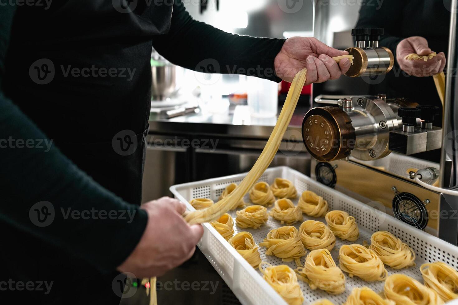 Close up male hands preparing fresh fettucine using machine inside pasta factory photo