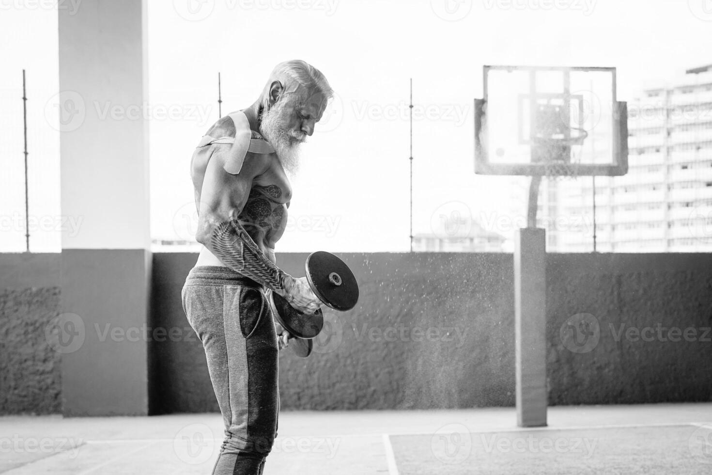 Senior fitness man doing biceps curl exercises inside old gym - Fit mature male training with dumbbells in wellness club center - Body building and sport healthy lifestyle concept photo