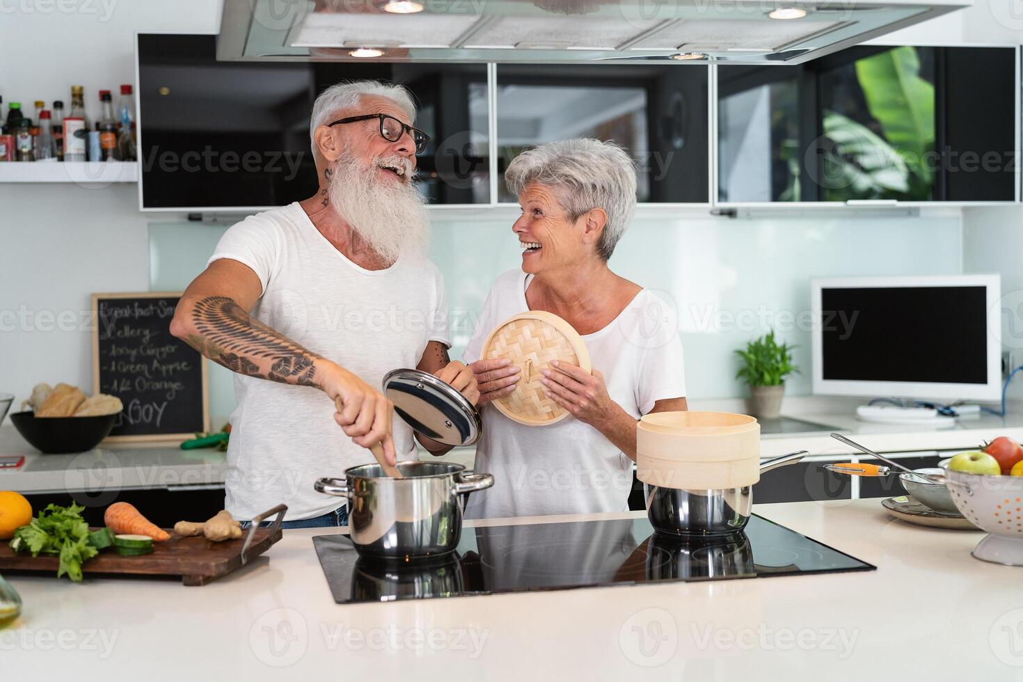 Happy senior couple having fun cooking together at home - Elderly people preparing health lunch in modern kitchen - Retired lifestyle family time and food nutrition concept photo