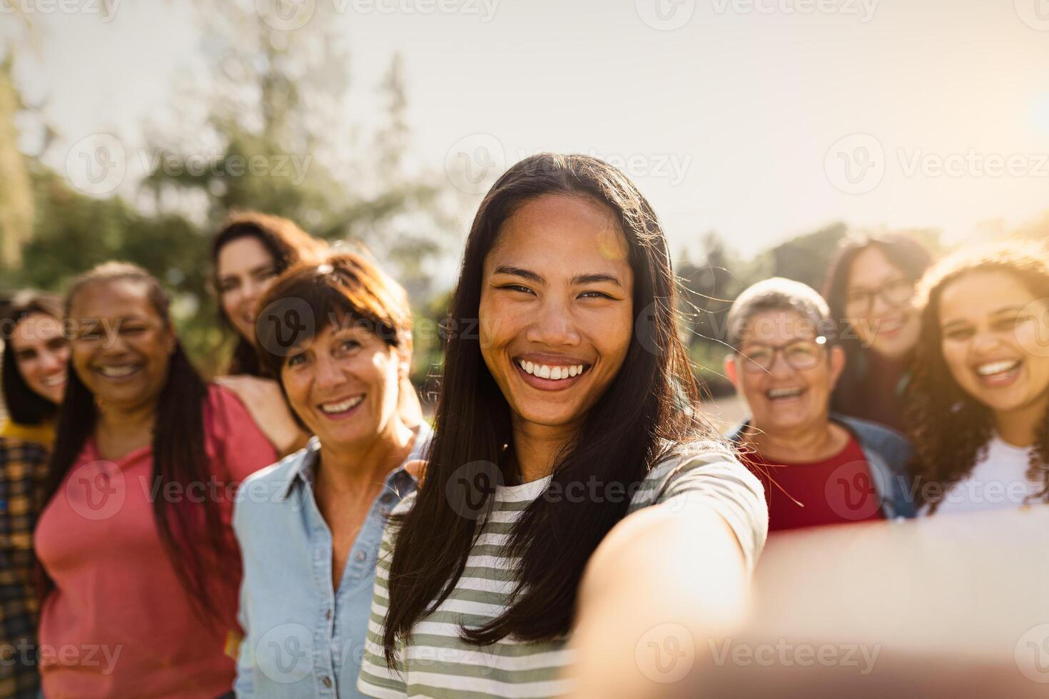 Happy multigenerational group of women with different ethnicities having fun taking selfie with smartphone camera in a public park - Females empowerment concept photo