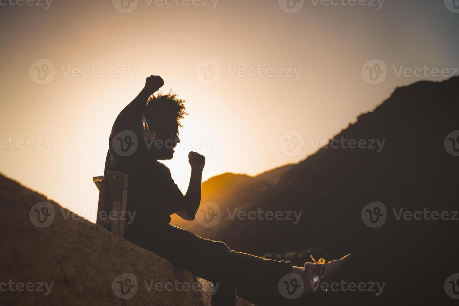 afro hombre teniendo divertido bailando y escuchando música con auriculares y Clásico boombox estéreo a puesta de sol hora durante vacaciones foto