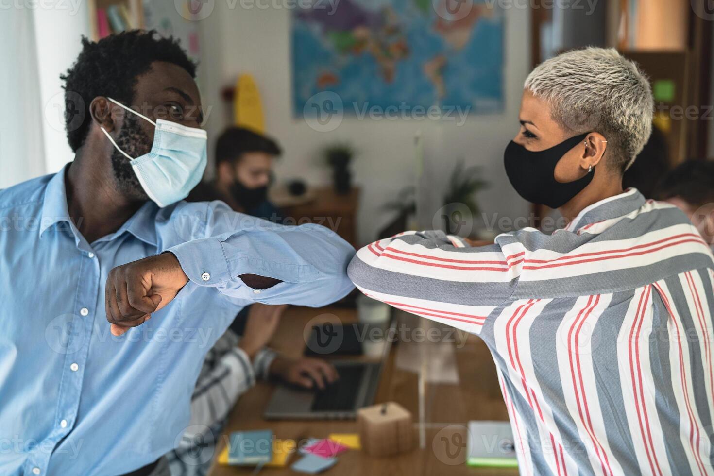 joven multirracial trabajadores vistiendo cara máscara haciendo nuevo social distancia saludos golpeando codos dentro trabajo colaborativo creativo espacio foto