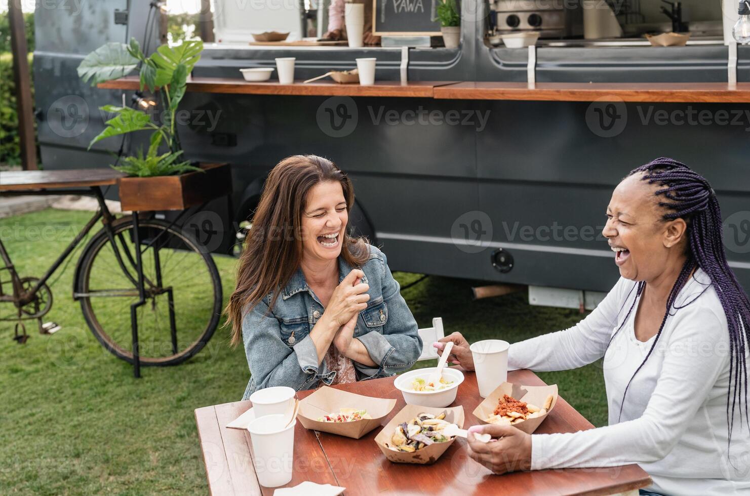 Happy multiracial senior friends having fun eating in a street food truck market photo
