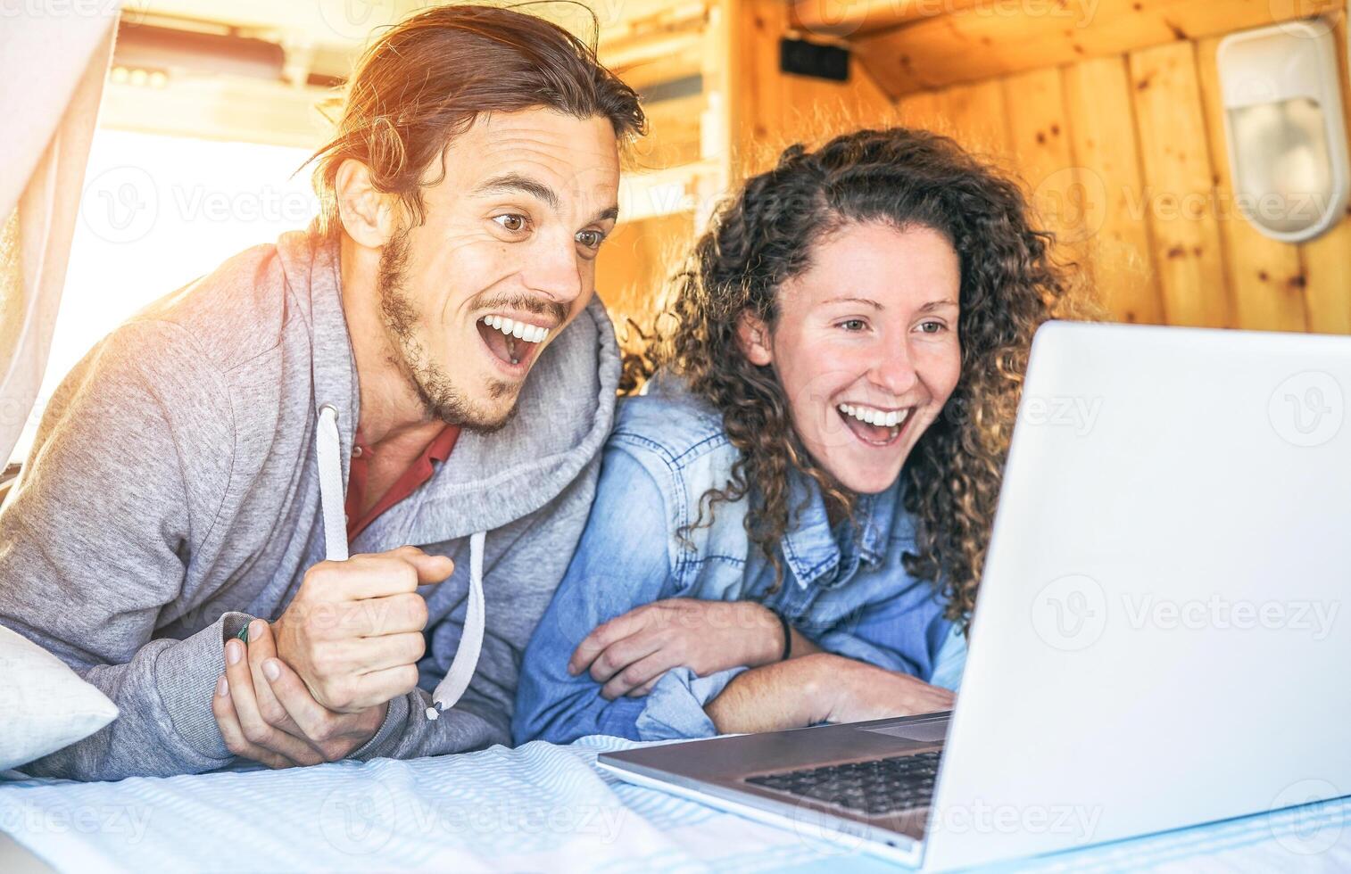 Happy man and woman watching surprised on their computer - Travel couple using laptop during their journey on a vintage minivan with wood interior - Vacation, love, technology concept photo