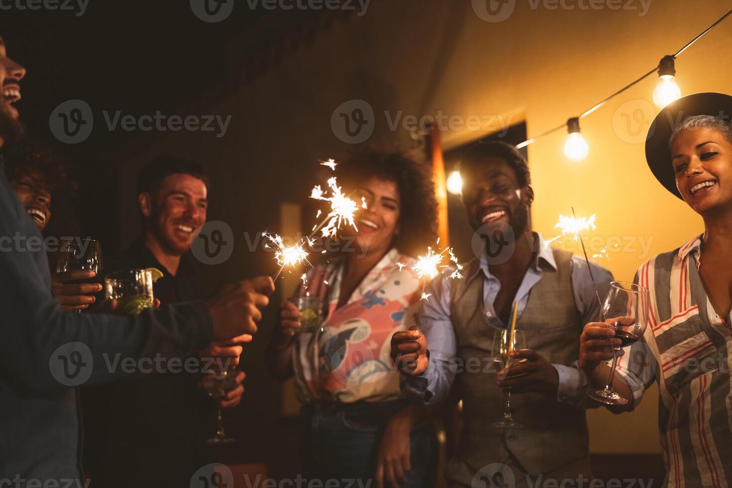 Happy young friends celebrating new year eve with sparklers fireworks and drinking cocktails on patio house party - Youth people lifestyle and holidays concept photo