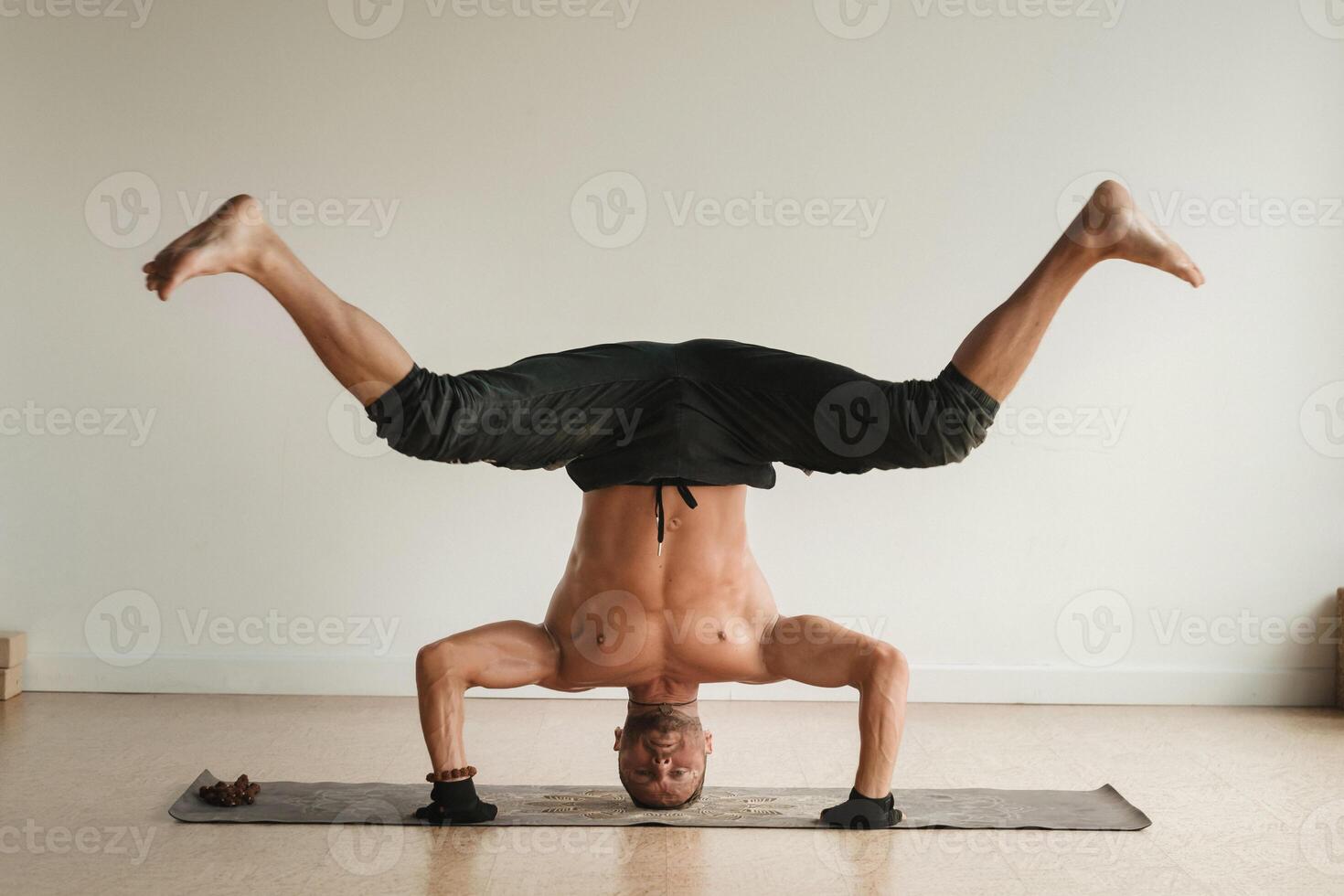 a man with a naked torso does yoga standing on his head indoors. Fitness Trainer photo