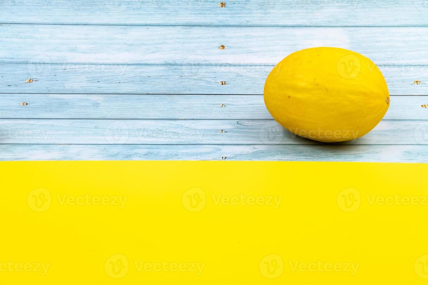 A whole yellow melon lies on a blue wooden background and a yellow background photo