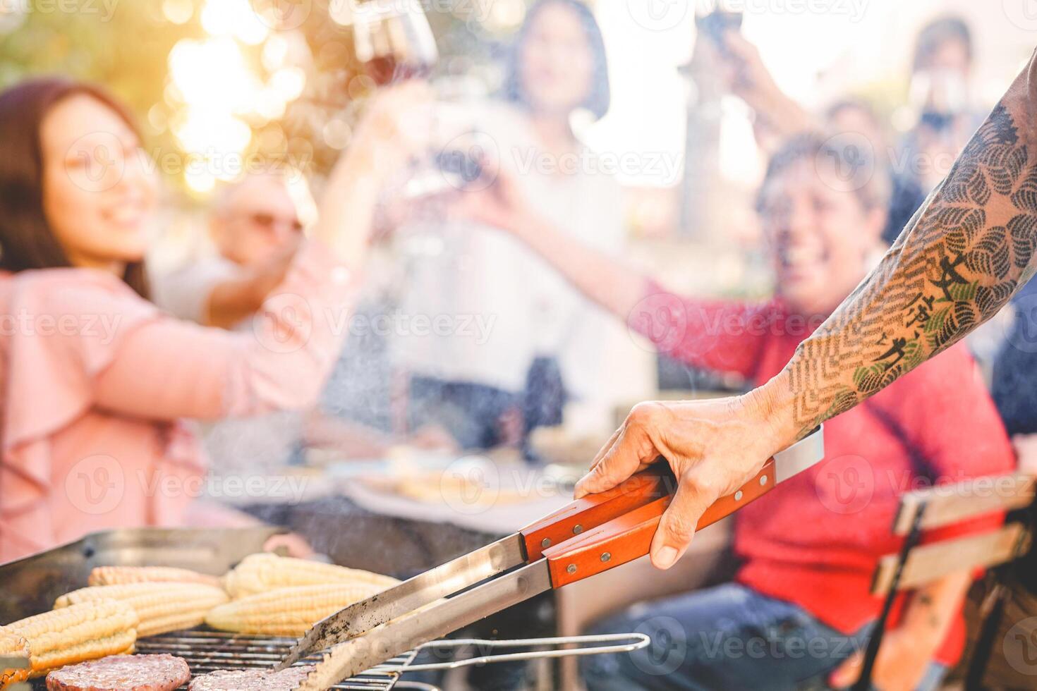 tatuado mayor hombre interrogatorio intenso hamburguesas para su familia a parilla cena fiesta - cerca arriba masculino mano Cocinando en barbacoa en el jardín - alimento, fin de semana actividades, diferente siglos y personas estilo de vida foto