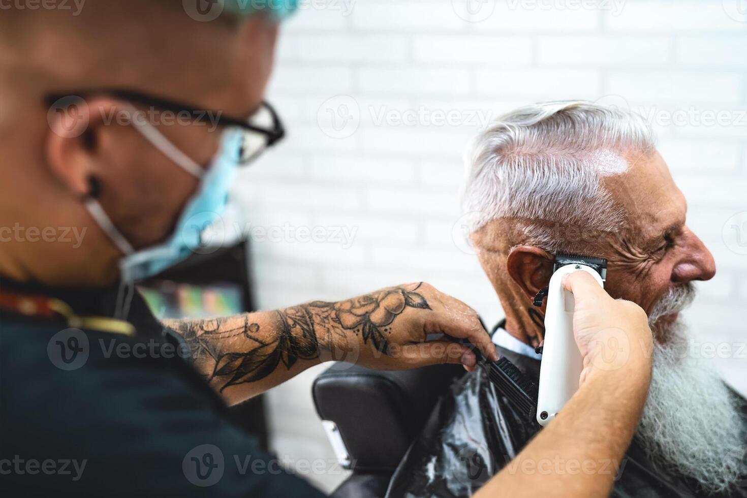 Male hairdresser cutting hair to hipster senior client while wearing face surgical mask - Young hairstylist working in barbershop during corona virus outbreak - Health care and haircut salon concept photo