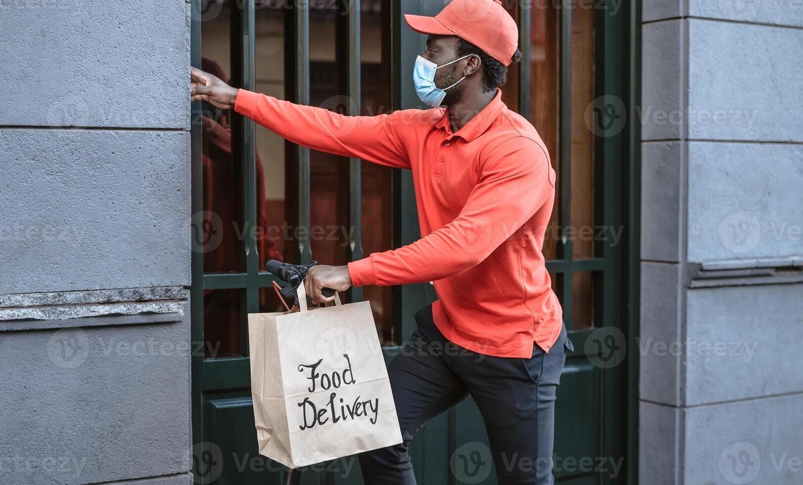 africano jinete hombre entregando comida a clientes con eléctrico scooter mientras vistiendo cara máscara durante corona virus brote - ecológico rápido entrega comida concepto foto