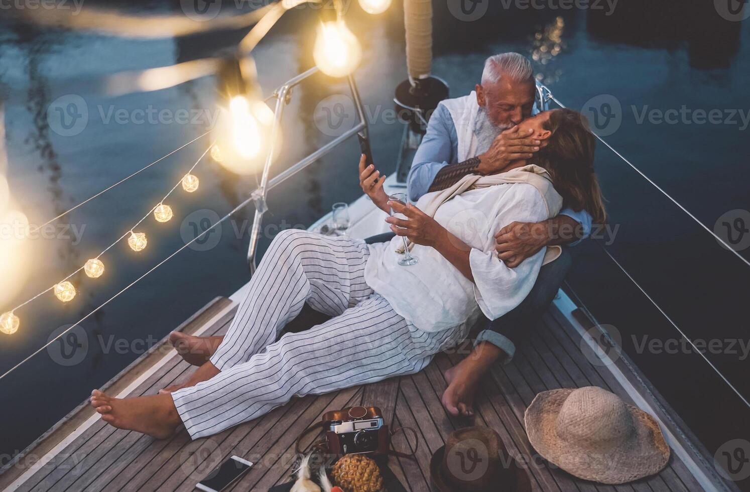 Senior couple kissing during sailboat vacation - Happy mature people having tender moments celebrating wedding anniversary on boat trip - Love relationship and travel lifestyle concept photo