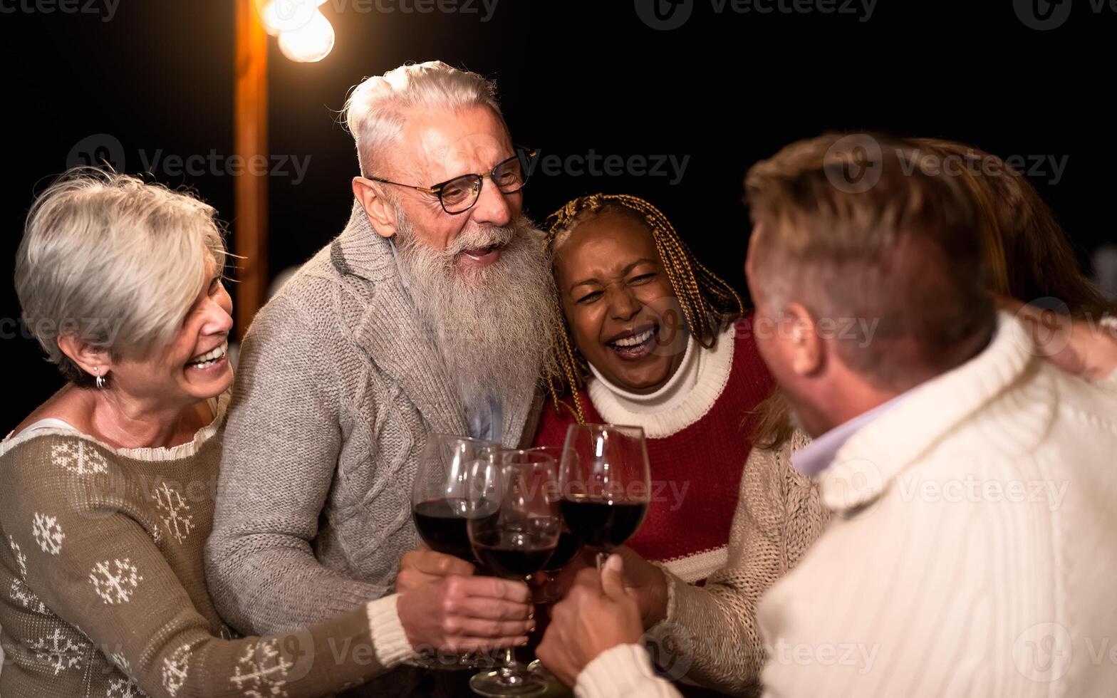 Happy senior friends celebrating holidays while toasting with red wine glasses on house patio party photo